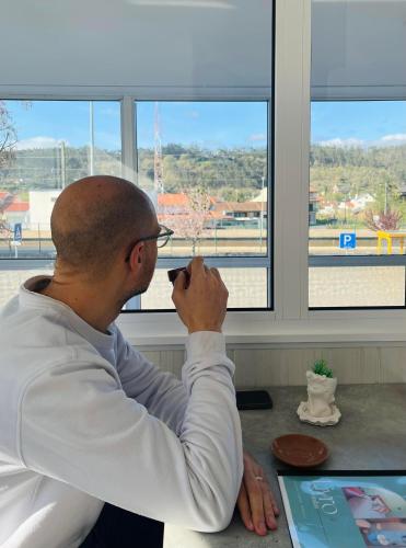 a man sitting at a desk looking out a window at Pensão Manalvo in Caxarias