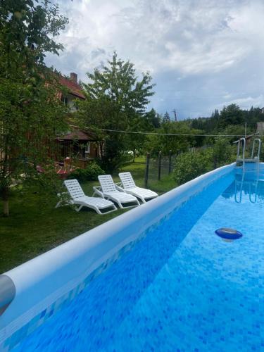una piscina con 2 sillas blancas al lado en Басейн з підігрівом! Batkivska Svitlitsa NEW Без господарів, en Slavske
