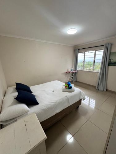 a bedroom with a bed with blue pillows and a window at 2 Bedroom Willow Park Apartment in Ballito