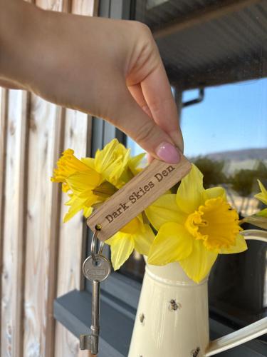 a hand holding a wooden key to a vase filled with flowers at Dark Skies den in Fryup