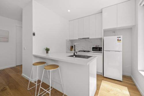 a white kitchen with two stools and a white refrigerator at Domi Rentals - The Moorabbin Townhouse in Moorabbin