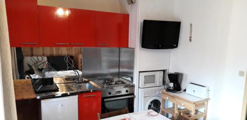 La cuisine est équipée de placards rouges et d'un four avec plaques de cuisson. dans l'établissement Résidence La Croix Du Sud - Studio cabine 4 personnes 2 exposé nord MAE-7924, à Valloire