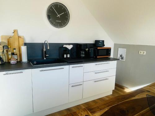 a kitchen with white cabinets and a clock on the wall at Ferienhaus Seenah - Wohnung Qualle in Großzössen