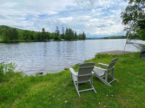 two chairs sitting on the grass next to a lake at Amazing lakefront home in the White Mountains with game room theater 51PR in Whitefield