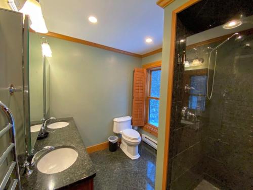 a bathroom with two sinks and a shower and a toilet at Amazing lakefront home in the White Mountains with game room theater 51PR in Whitefield