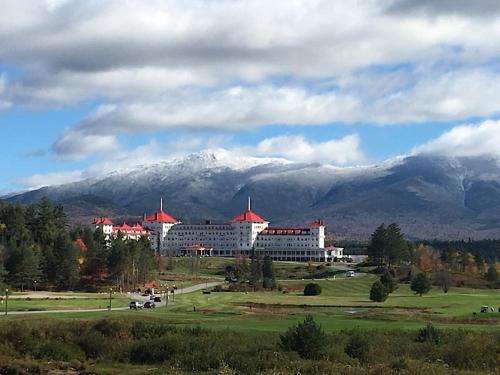 a large building with red roofs in front of a mountain at Amazing lakefront home in the White Mountains with game room theater 51PR in Whitefield