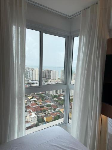 a bedroom with a large window with white curtains at Apart Moderno Proximo ao Mar in Vila Velha
