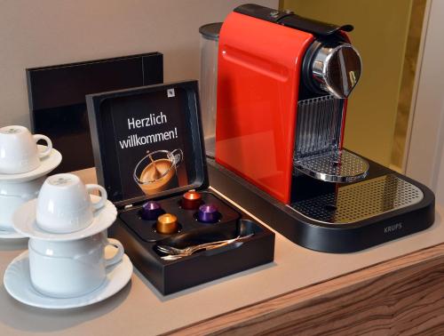 a red and black coffee maker and cups on a counter at Best Western Plus Delta Park Hotel in Mannheim