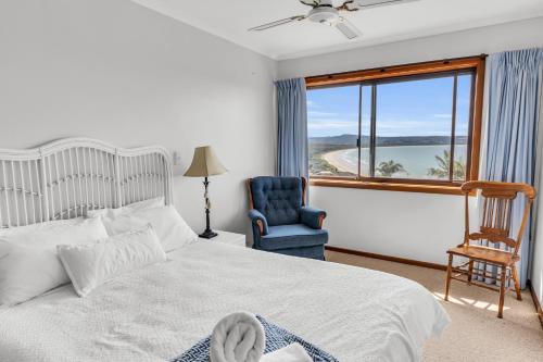 a bedroom with a bed and a chair and a window at Waves on Winnunga in Pambula Beach