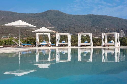 a pool with chairs and umbrellas next to a mountain at Susona Bodrum, LXR Hotels & Resorts in Torba
