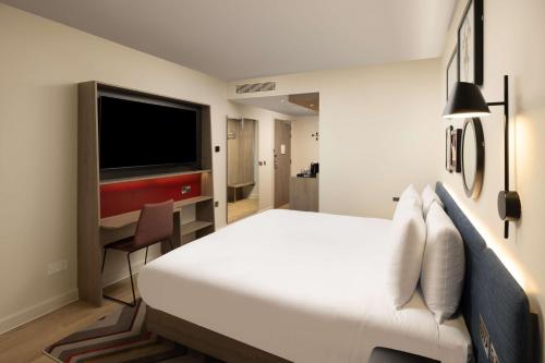 a bedroom with a bed and a desk with a television at Hampton By Hilton London City in London