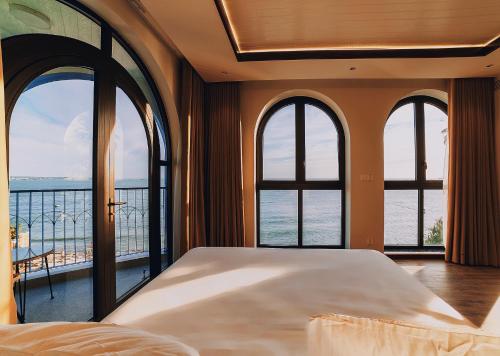 a bedroom with a large bed and large windows at LCV Mũi Né Resort in Mui Ne