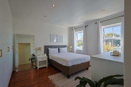 a bedroom with a large bed and two windows at Fully Equipped Claremont Home with Pool & Style in Cape Town