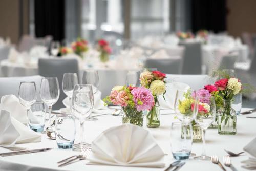 a table with glasses and vases with flowers on it at Hilton Cologne in Cologne