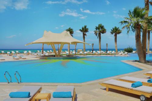 a large swimming pool with chairs and palm trees at Hilton Hurghada Plaza Hotel in Hurghada