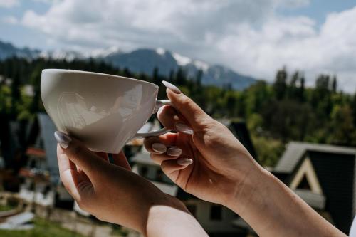 a person holding a white cup in their hands at Gościna u Maryny & SPA pod Tatrami in Poronin