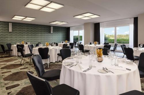 a banquet room with white tables and chairs and windows at Hilton Vienna Waterfront in Vienna