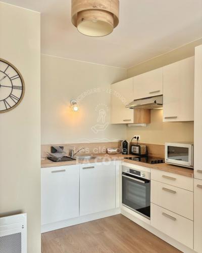 une cuisine avec des placards blancs et une horloge murale dans l'établissement La Petite Plage, à Merlimont