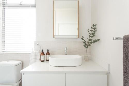 a white bathroom with a sink and a mirror at 1 Bedroom Muizenberg Beach Apartment with Pool and Mountain Views in Muizenberg