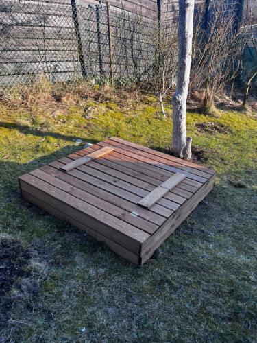 a wooden platform sitting on the grass next to a tree at A&R Kaszuby Natura Dom Wypoczynek in Gowidlino