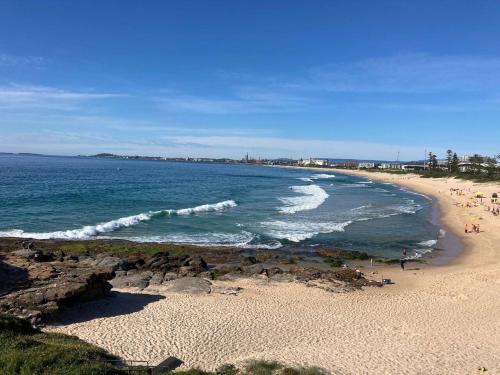 a beach with people walking on the sand and the ocean at Arena Beach Escape - Smart Urban Stay near Stadium in Wollongong