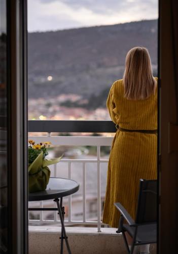a woman in a yellow dress looking out a window at LakeSide Apartment in Kastoria