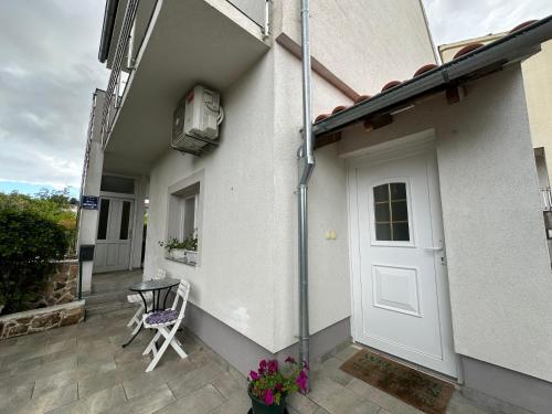 a white house with a door and a chair on a patio at Apartman Lena in Bilice