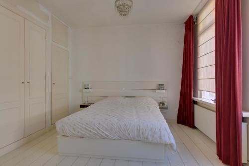 a white bedroom with a bed and a red curtain at Casa Hofdijkstraat in Alkmaar