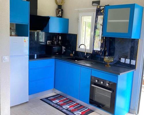 a blue kitchen with blue cabinets and a refrigerator at Bungalow au pied de la Soufrière in Saint-Claude