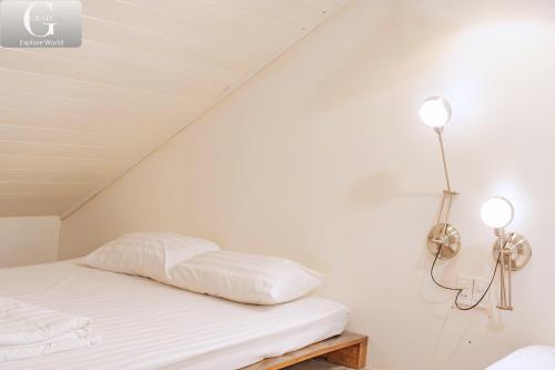 a bed with white sheets and two lights on the wall at Hoang Yen Villa & Coffee in Da Lat