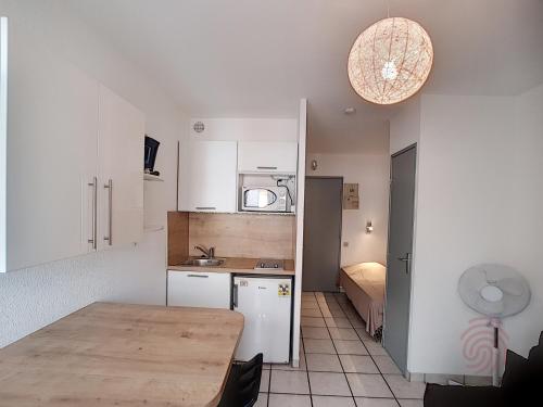 une cuisine avec des placards blancs et une table ainsi qu'une chambre dans l'établissement Studio rénové avec balcon, proche des Thermes de Lamalou, animaux acceptés, parking gratuit. - FR-1-451-131, à Lamalou-les-Bains
