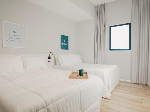 two white beds in a white room with a table at Apê Santos Praia do Gonzaga in Santos