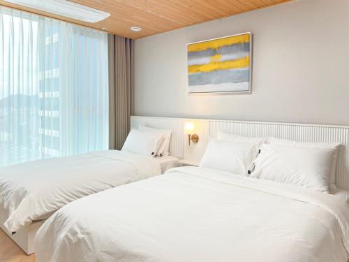 two white beds in a room with a window at Brown Suites Busan Station in Busan
