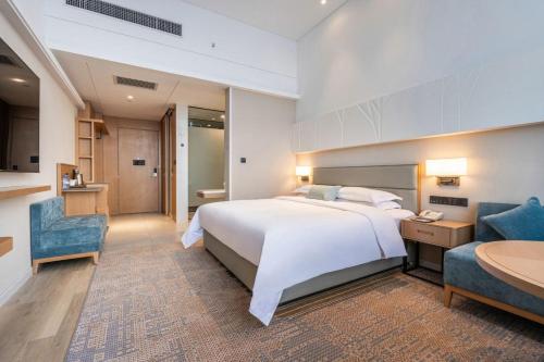 a bedroom with a large white bed and two blue chairs at Xianyang Licai Tianyou Hotel in Xianyang