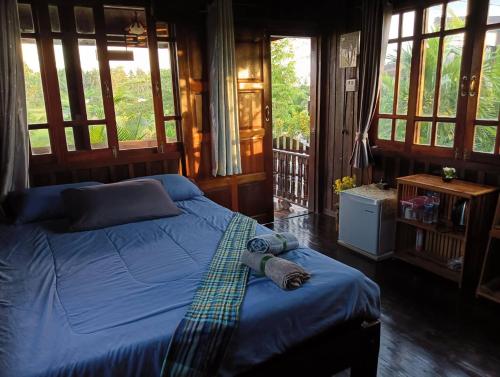 a bedroom with a bed with blue sheets and windows at สุขเสมอ โฮมสเตย์ (Suk-Samer homestay) in Ban Nong Phao Than