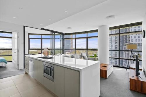 a kitchen with a counter and a living room with windows at 105OP Abnb-Style Spectacular Park View 2BR Apt with Free Parking in Sydney