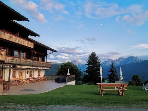 a building with a bench and tables and mountains at Lienharterhof in Monguelfo