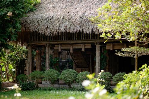 a building with a thatched roof with plants and trees at Dinh Gia Trang - Homestay & Coffee in Yên Bái