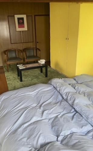 an unmade bed in a room with a table and chairs at 古民家ゲストハウス穏 in Sakaide