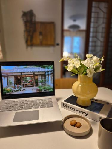 a laptop computer sitting on a table with a vase of flowers at Live in Busan Stay Gwangalli in Busan