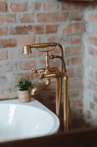 a bathroom sink with a gold faucet next to a brick wall at História Présház boutique Nagyréde in Gyöngyös