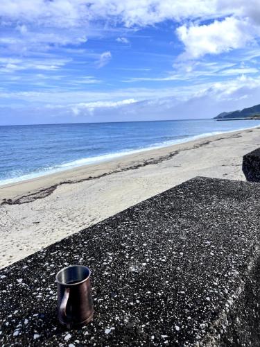 a metal cup sitting on a beach next to the ocean at NagataSeaTime in Yakushima
