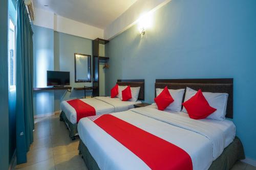 two beds in a hotel room with red pillows at Hotel O Hotel Orchard Inn in Lumut