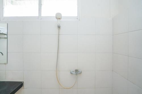 a shower in a white tiled bathroom with a window at Capital O 1430 Hotel Ratna Syariah in Probolinggo