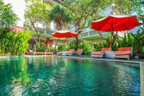 a swimming pool with umbrellas and chairs next to a building at Capital O 1666 Grand Pudjawan Hotel Near Kuta Beach in Kuta