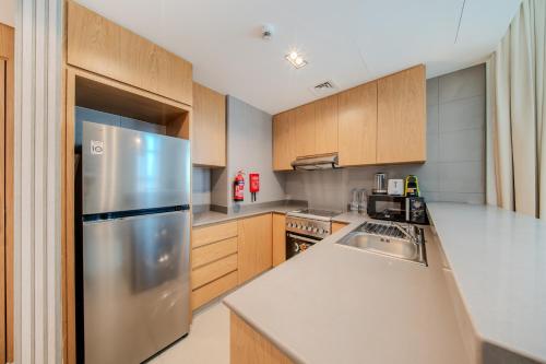 a kitchen with a stainless steel refrigerator and wooden cabinets at 1BR The Golden Souq by Blue Cloud Holidays in Sharjah Intl