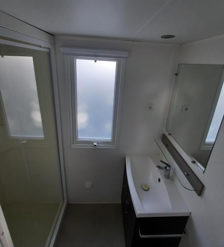 La salle de bains est pourvue d'un lavabo, d'une fenêtre et d'un miroir. dans l'établissement Mobil Home Charente-Maritime camping LA PIGNADE, à La Tremblade