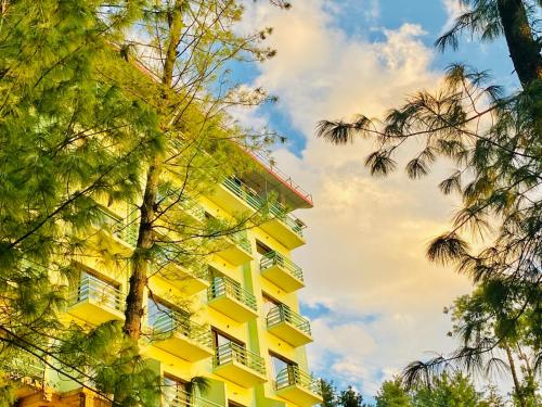 a yellow building with white windows and trees at Aachman Nature Valley Resort Mashobra BY NAINA STAYCATION- Private Parking - Balcony and valley view Rooms in Shimla