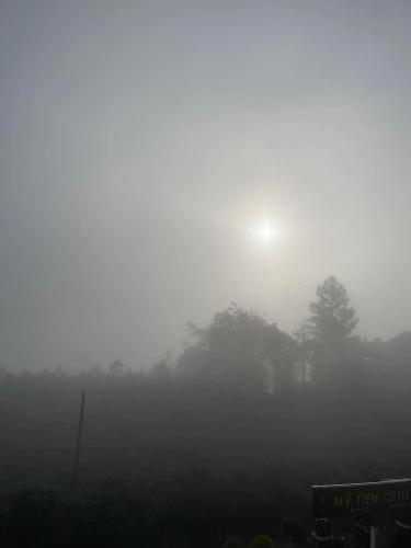 a foggy field with trees and the sun in the background at Mỹ Tiên Homestay in Blao Srê