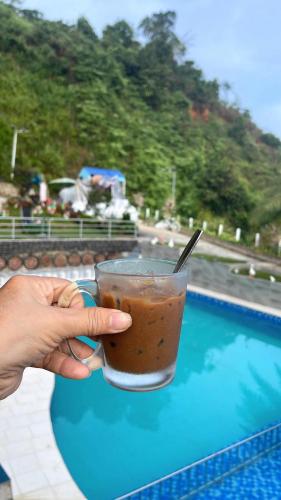 a person holding a drink in a cup next to a pool at Mỹ Tiên Homestay in Blao Srê